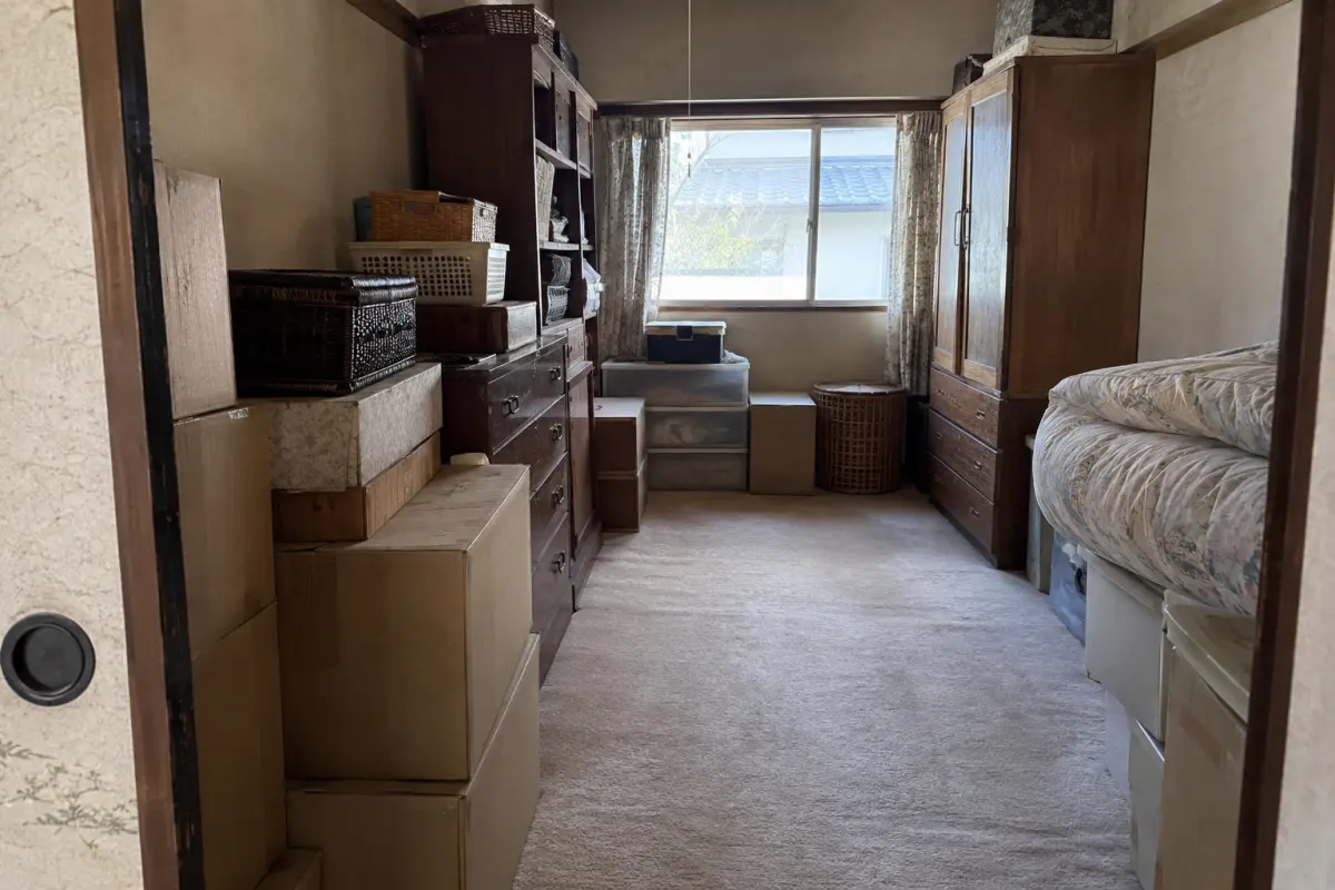 古い室内の入口から、棚、箱、家具、布団と窓の位置関係が見える生成画像