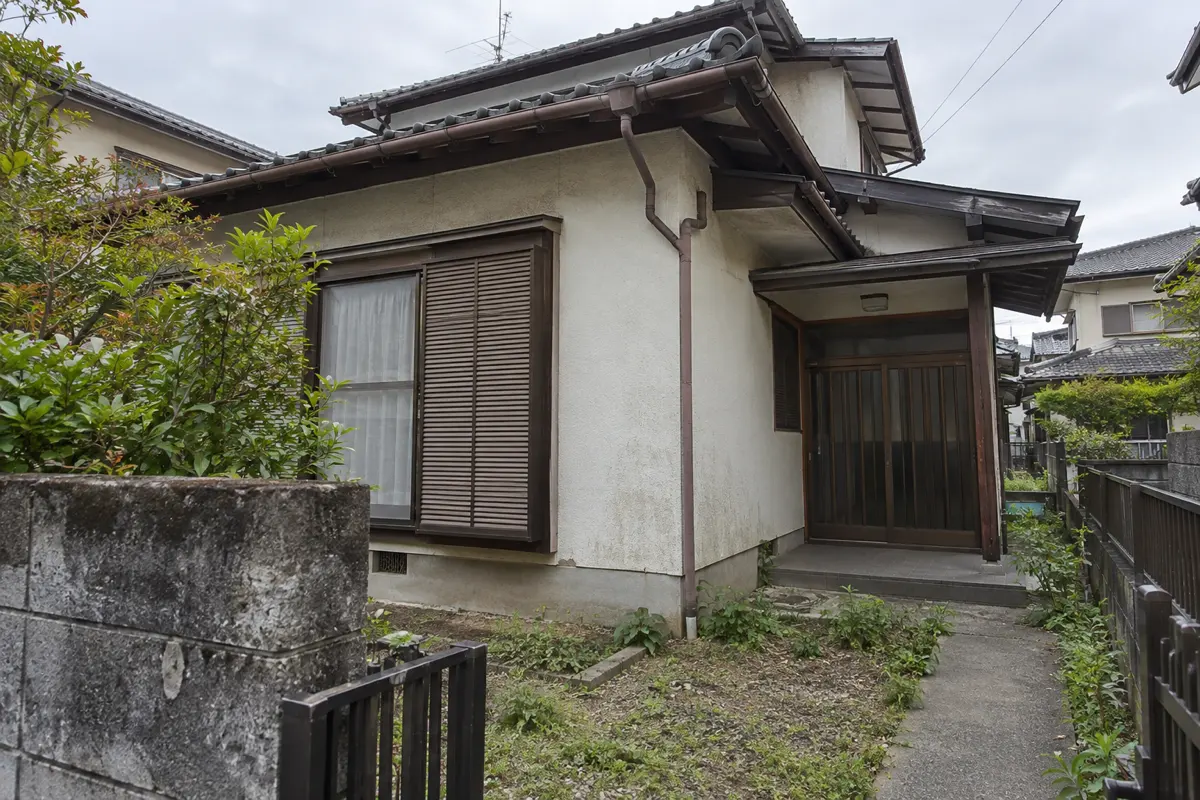 古い日本家屋の外観。軒と雨樋、壁、玄関までの通路が見える説明用画像