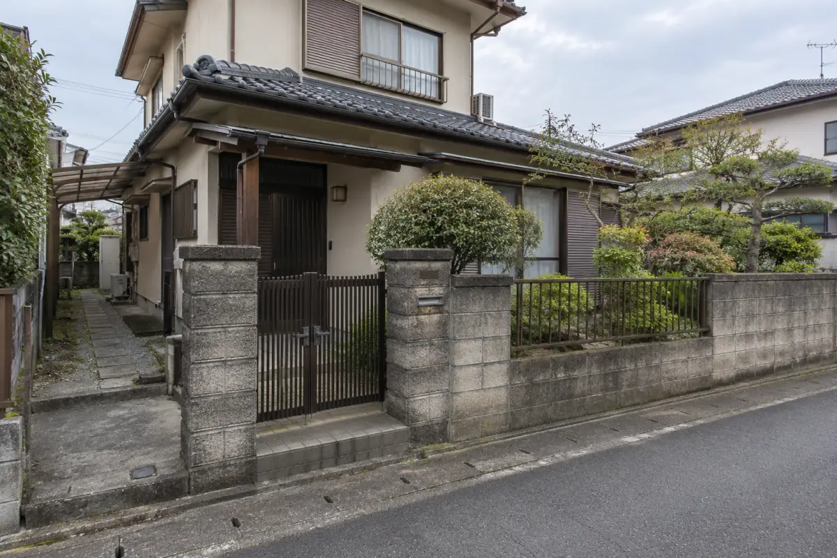 道路から見た古い日本の戸建て住宅の外壁と門、庭木を描いた説明用生成写真