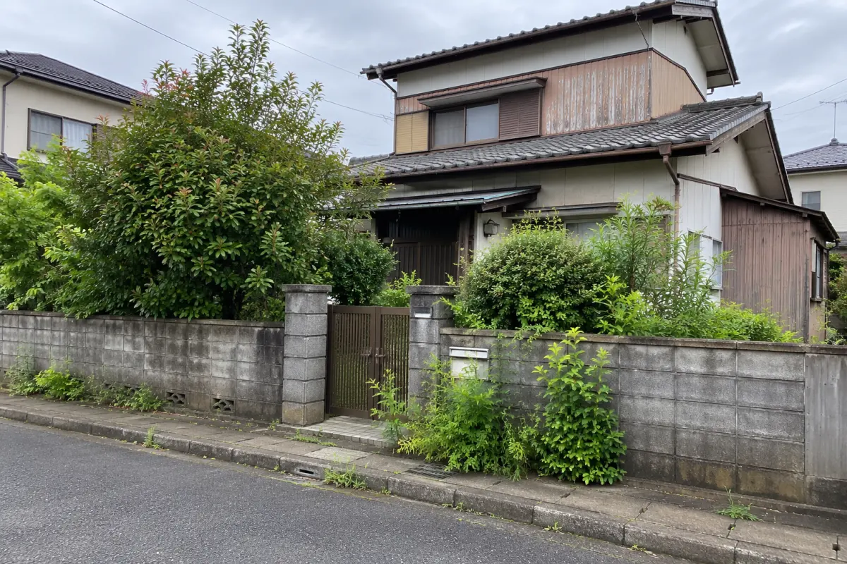 庭木が伸びた古い日本の戸建て住宅を公道側から見た説明用生成写真