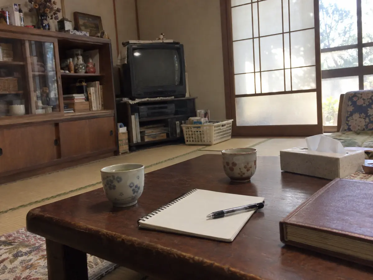 古い家の居間の座卓に、無記名のノートと筆記具、湯のみを置いた編集用の生成写真