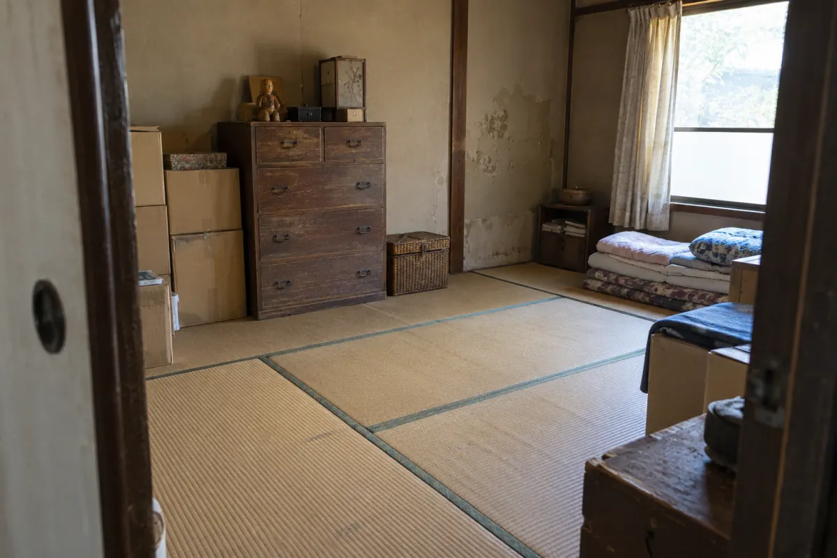 古い日本の和室を入口から写した説明用生成写真。箪笥、箱、布団が残り、壁と畳が見える