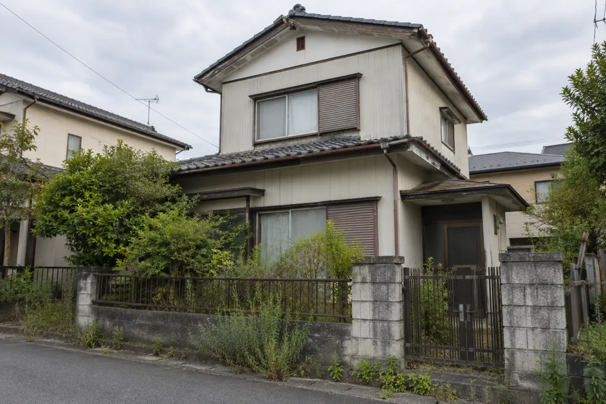 道路側から見た古い日本の戸建て住宅の外観。門、庭木、窓、屋根の見える範囲を示す説明用生成写真
