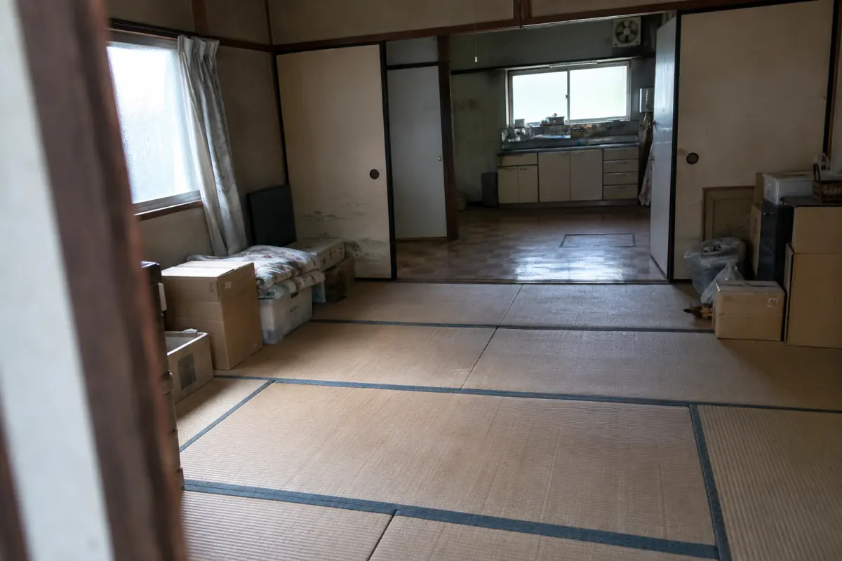 古い和室の入口から台所までを写した説明用画像。畳、建具、室内の動線と壁際の家財が見える