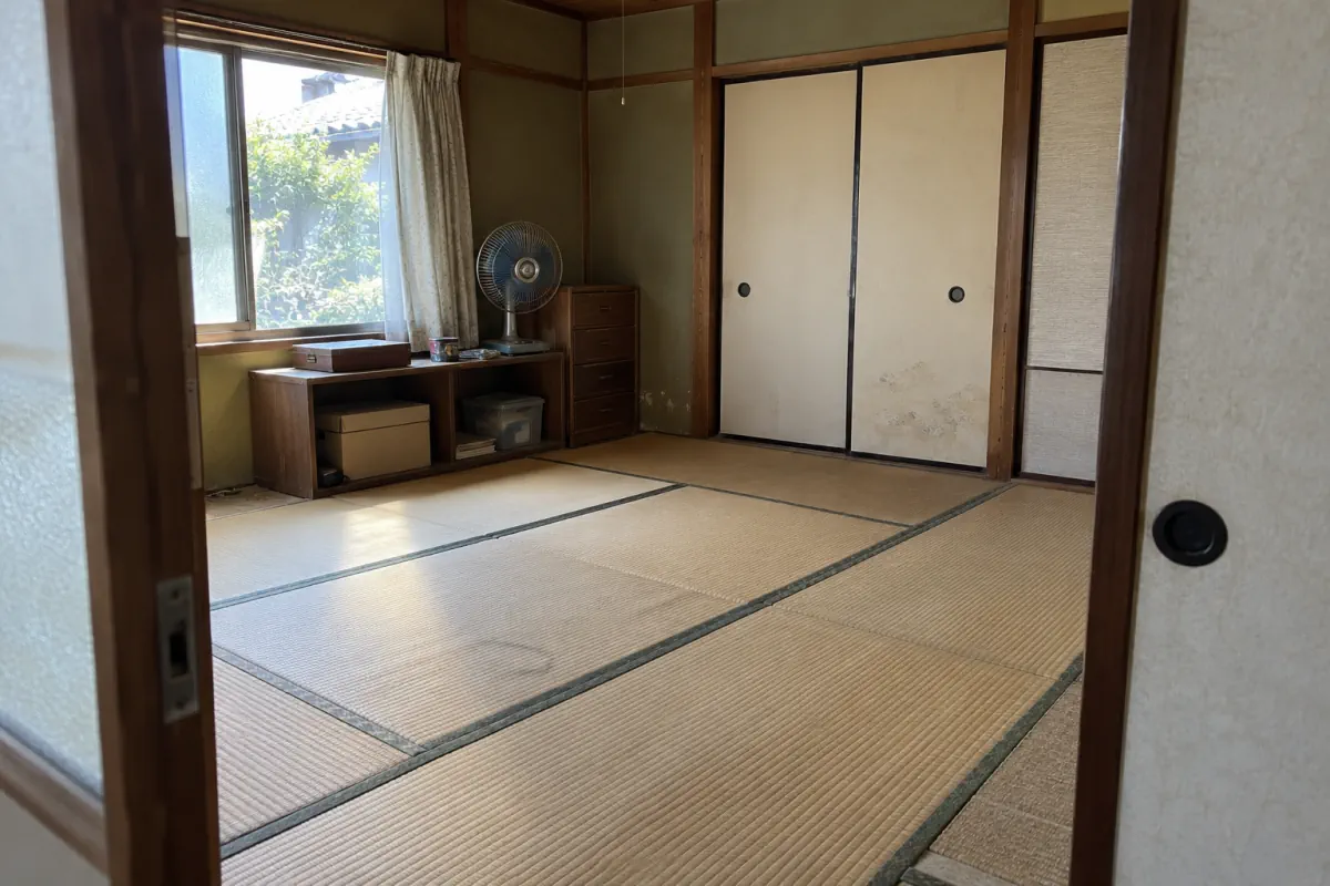 古い日本の住宅の和室を入口から写した説明用生成写真。畳、襖、窓、残る棚が見える
