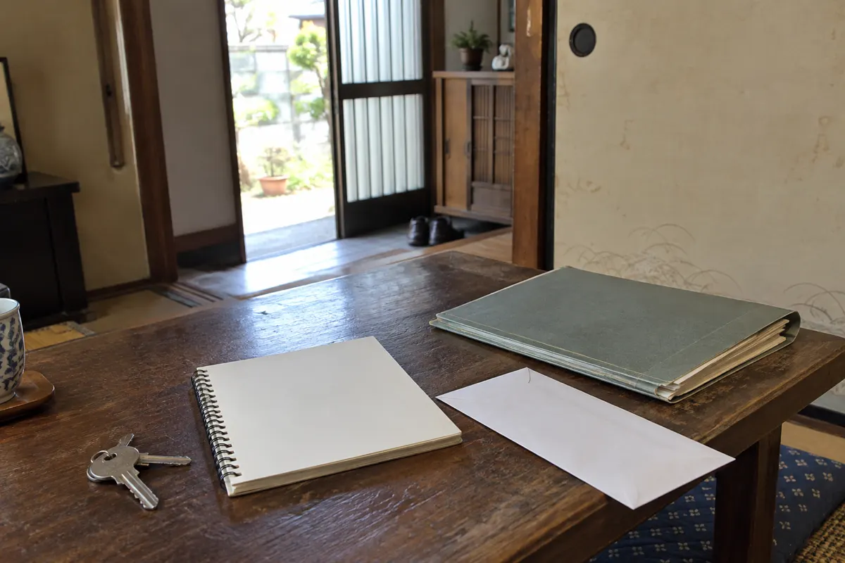 古い家の食卓に鍵、無記名のノート、封筒、書類袋を置いた生成写真