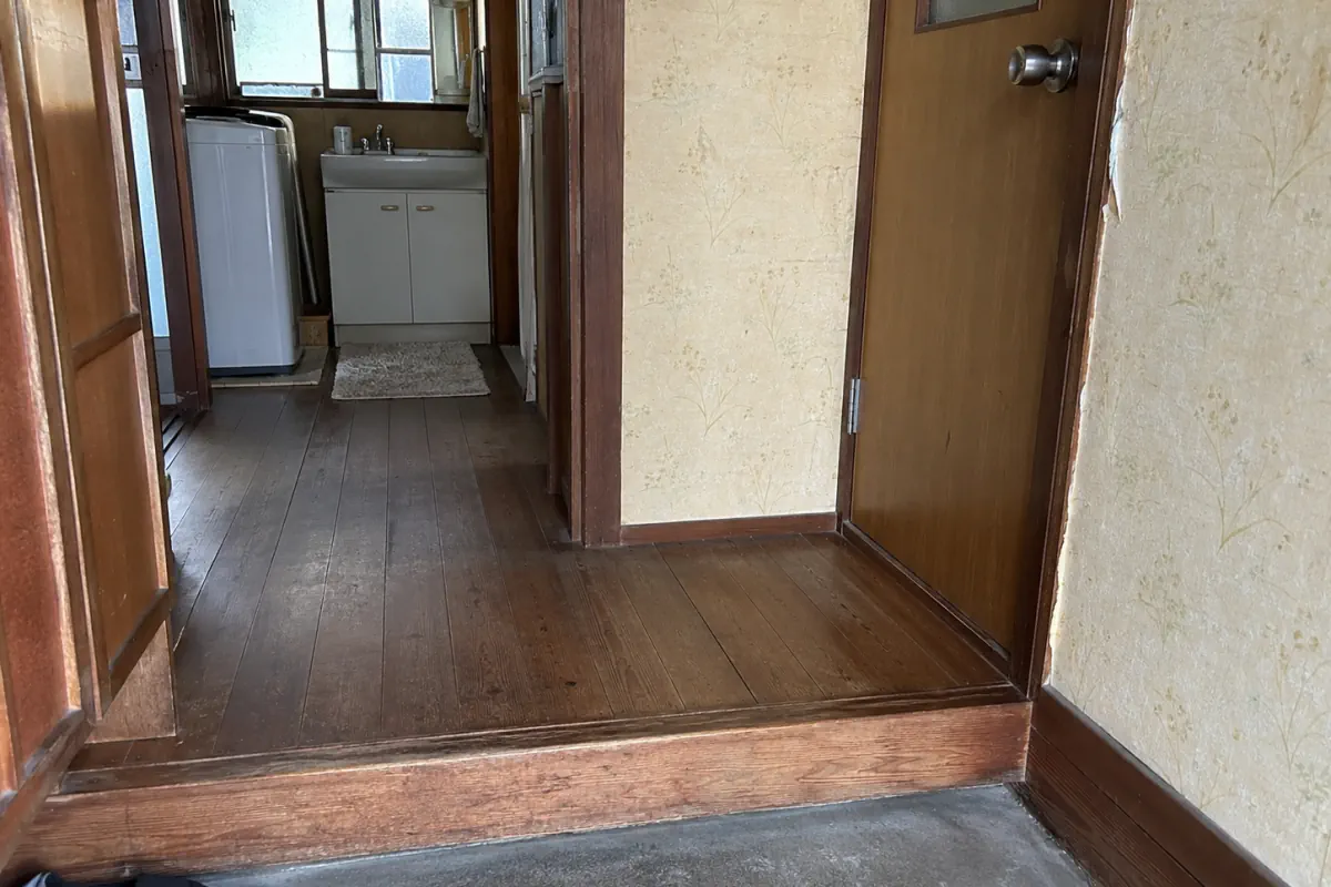 古い日本の住宅の玄関から洗面所へ続く廊下と木の段差を少し斜めに写した説明用生成写真