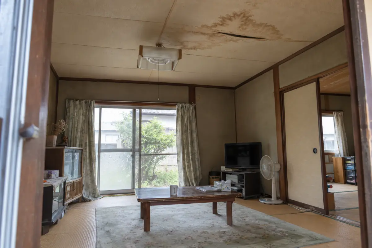 古い日本家屋の部屋を入口から見た構図。天井に広がる染みと開いた継ぎ目を示す説明用の生成画像