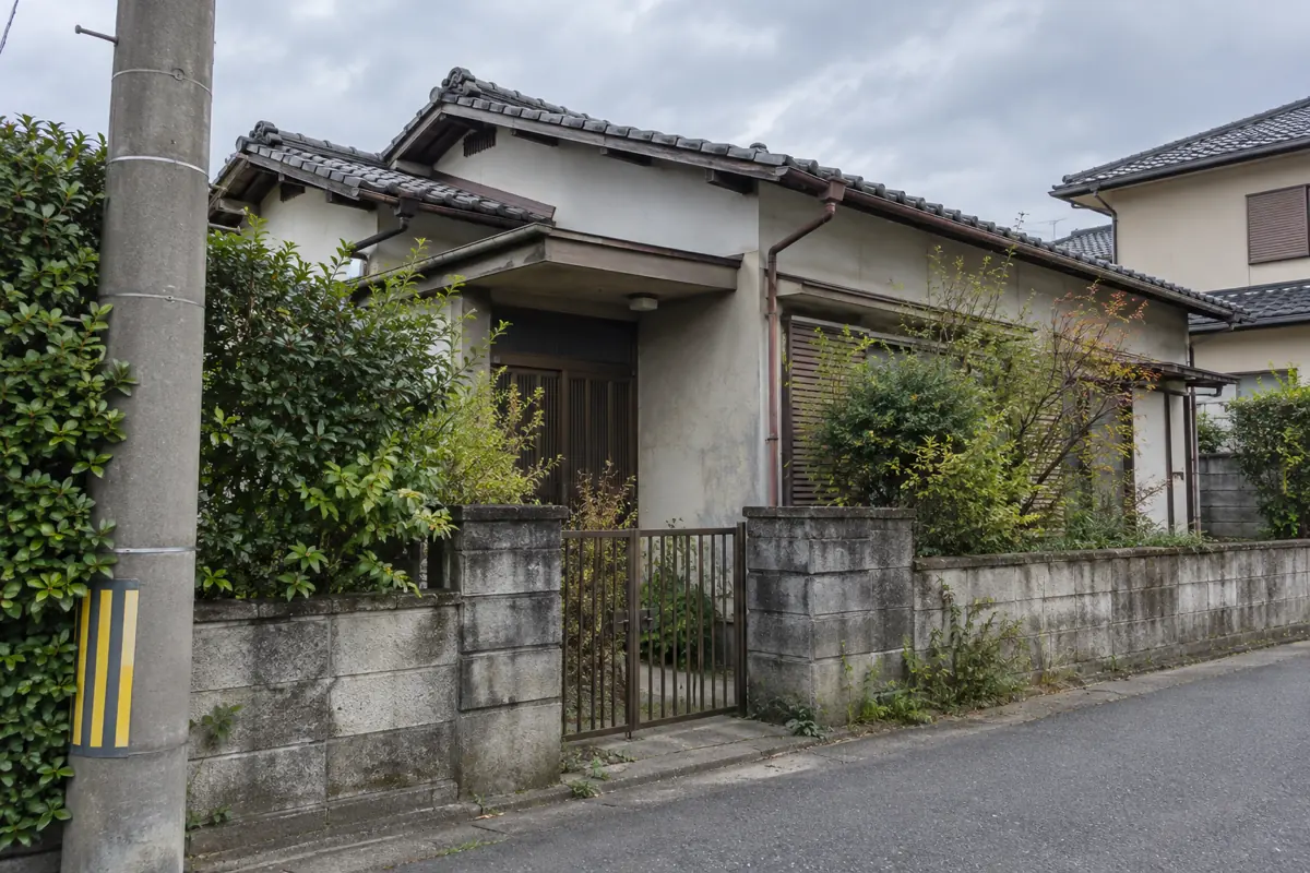 道路側から見た古い日本の家の説明用画像。瓦屋根、門、庭木と道路が写る