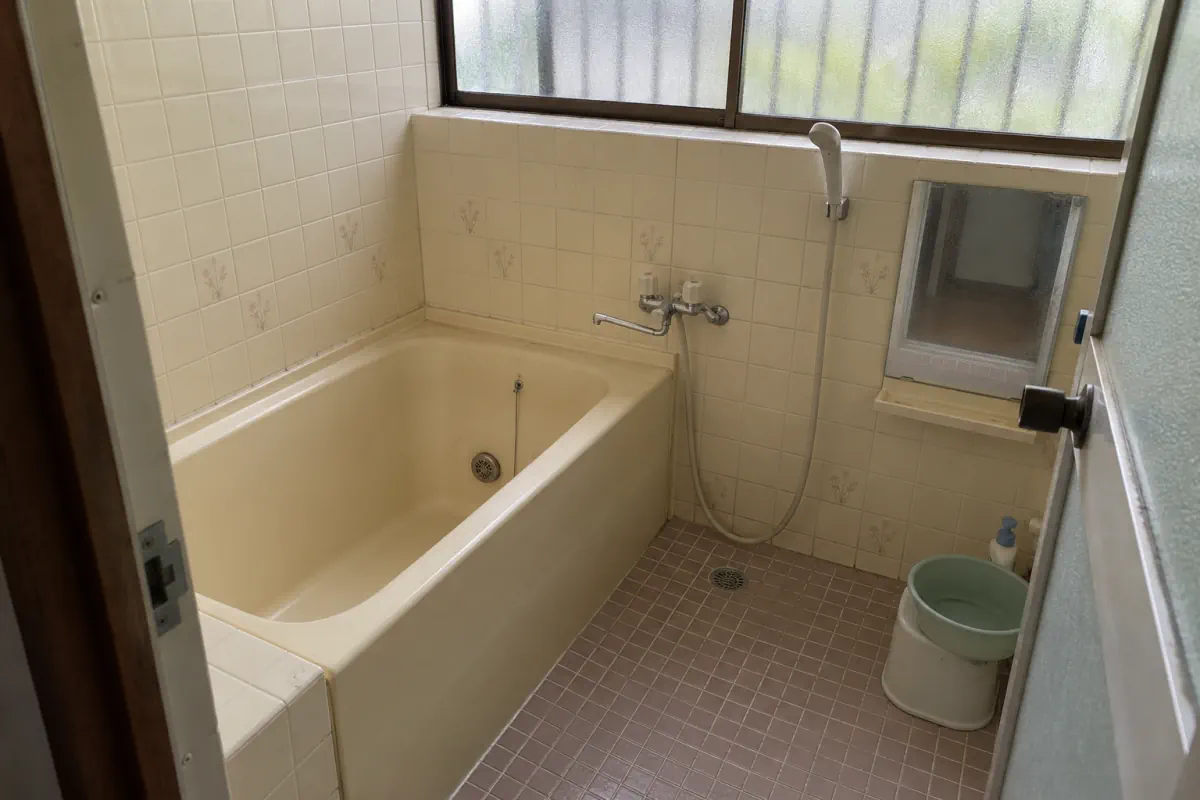 古い日本の住宅の浴室を入口から写した説明用生成写真。浴槽、壁、床、給排水の位置が見える